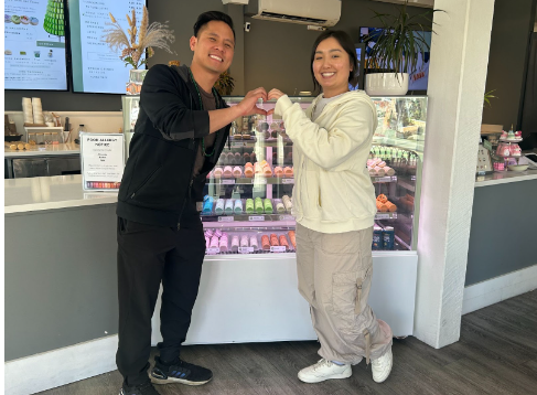 Picture of business owner Michael Huynh and employee Jemmy making a heart sign in front of their flavorful display of macarons. (Photo by Janiyah Gibson).       