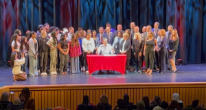 A photo of the Governor singing his campaign with students and staff behind him. 