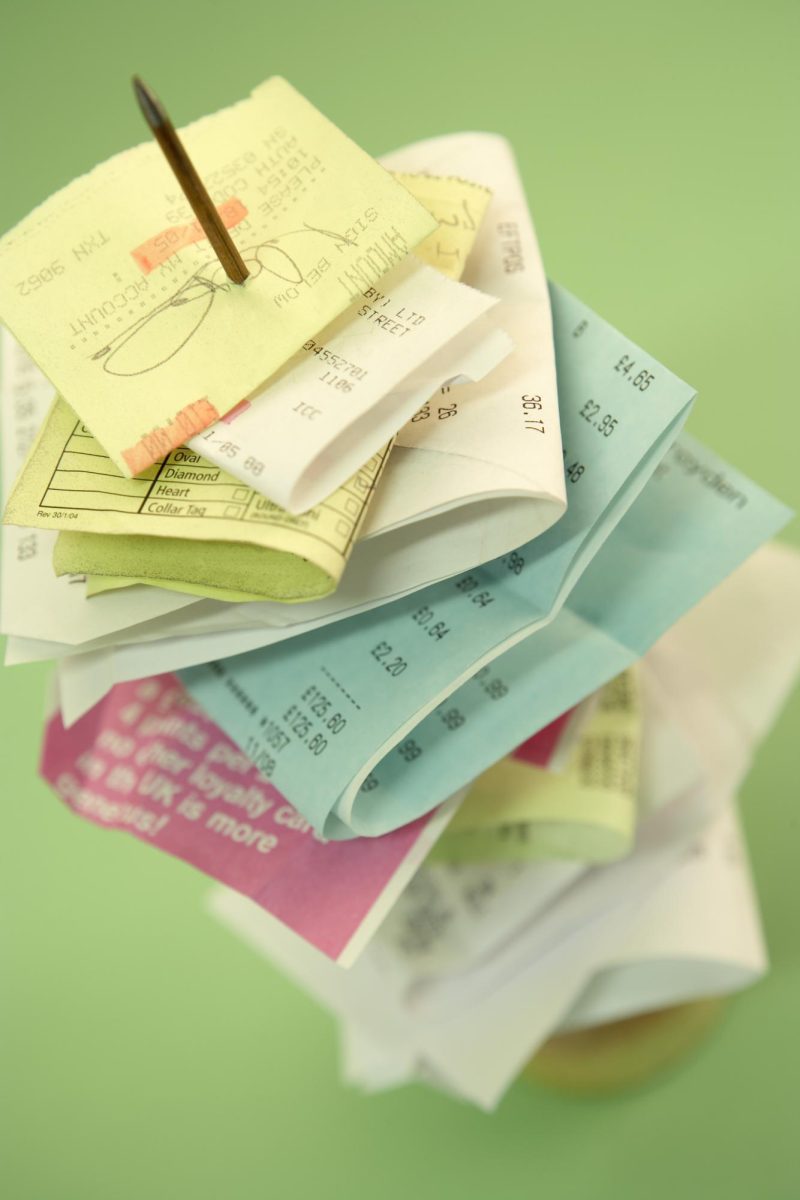 Picture of a stack of various receipts, secured with a pin, on a light green surface. (https://www.freeimages.com/photo/notes-stacked-together-1687711).