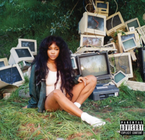 A photo of SZA's album cover featuring her in a white top and blue jacket sitting in front of old 90's TVs and computer monitors. 