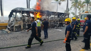 Photo of firefighters with a burnt down bus behind them.