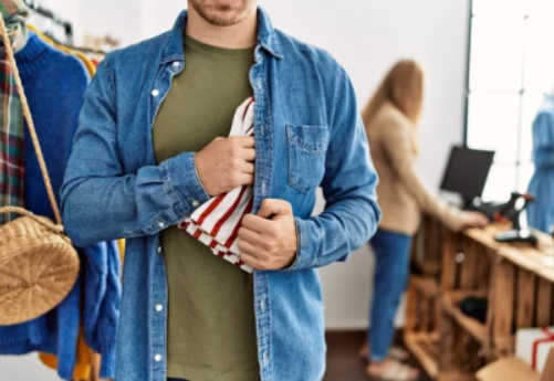 Photo of a man stuffing something into his jacket, implicating retail theft.